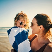 Mother wraps child in towel on beach
